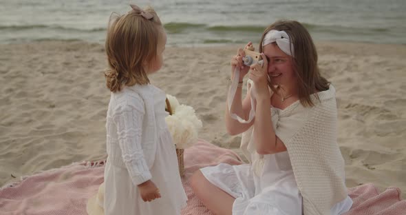 Mother and Baby Daughter Sit on the Beach Near the Sea Playing Together