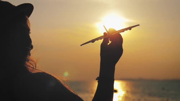 Silhouette Girl Plays with a Toy Airplane on Tropical Beach at Sunset. Hand with Small Plane Close