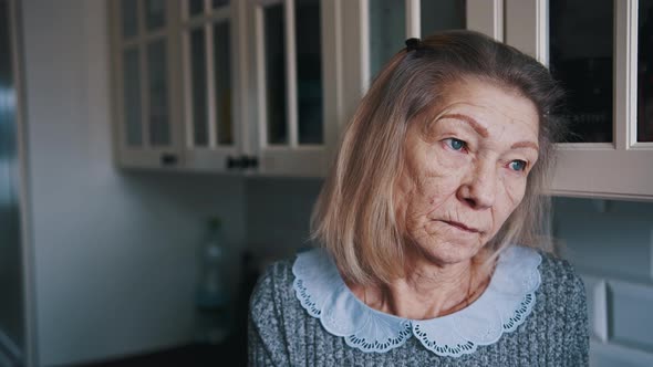 Portrait of Elderly Gray Haired Lady Looking Through the Kitchen Window and Thinking