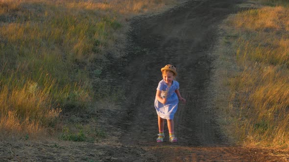 Adorable little girl in blue summer dress climbing up the hill. Child running in wild grass country