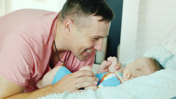 Young Father Smiling Happily To His Baby. He Looks at It