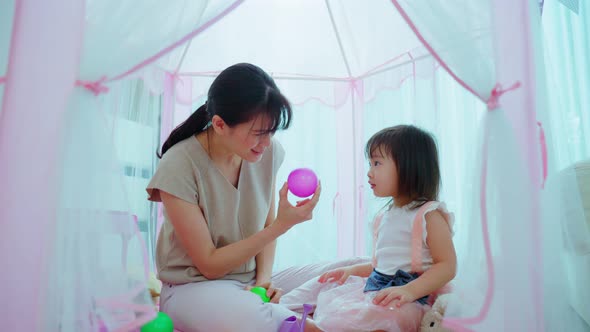 Asian mother teach young girl daughter about color in tent at home help kid to develop skill.