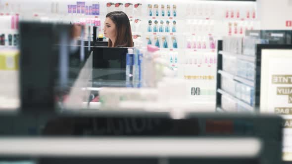 Side View of Young Caucasian Woman Walks Past Stalls in Cosmetics Store