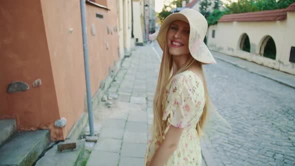 Smiling Woman Walking on Street. Cheerful Pretty Girl in White Hat Looking Back at Camera While