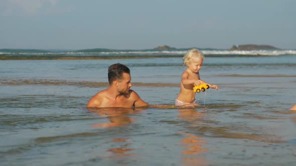 Child Plays Holding Toy and Swimming in Ocean with Parents