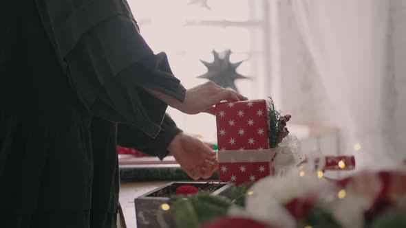 A Young Woman Packs a Christmas Present in Red Paper and Ties It with Ribbons