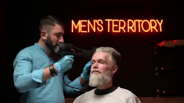 The master in the barbershop makes stylish styling for an adult gray-haired man