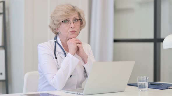 Pensive Old Female Doctor Thinking and Working on Laptop
