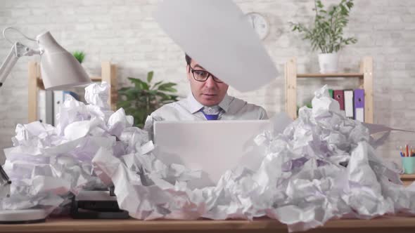 Male Office Worker Has a Lot of Work Sitting at a Laptop in a Heaps of Papers Slow Mo