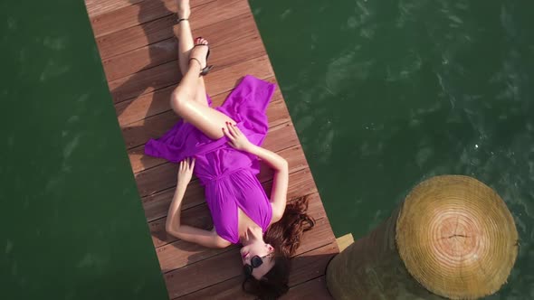 Aerial View of Young Sexy Woman in Purple Dress Lying on Wooden Dock Above Sea