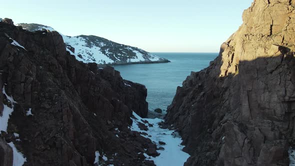 Winter Aerial Flight Through Scenic Canyon Top Over Waves Rolling on Artic Ocean Shore with Round