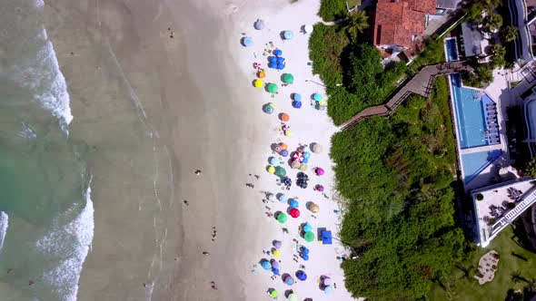 Aerial top down view of Bombinhas beach with people and umbrellas and a hill on the right