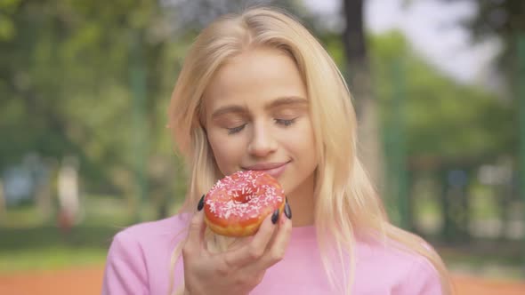 Portrait of Cheerful Blond Woman Biting Sweet Donut and Laughing. Happy Beautiful Caucasian Lady