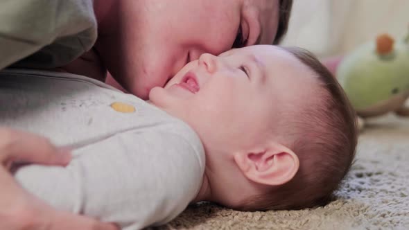 The mother kisses the happy laughing baby and hugs him. Mom amuses a smiling, happy child