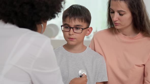 Afro American Woman Doctor Listens to Child's Lungs Using Stethoscope During Checkup