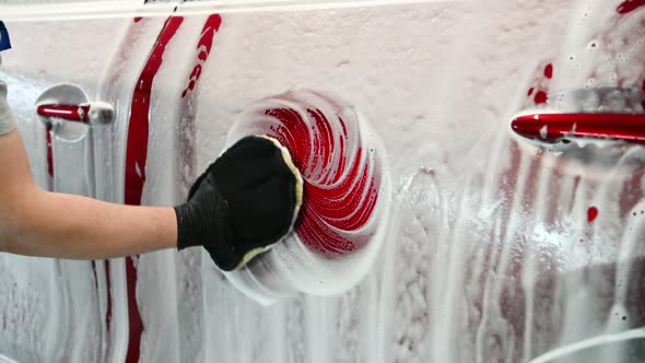 A Man Making Manual Car Wash on a Red Car with Special Cleaning Glove