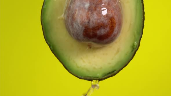 Water falling from avocado on yellow background. Avocado slice and water splashing, drops of juice