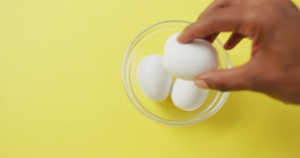 Video of close up of biracial man putting egg into bowl on yellow background