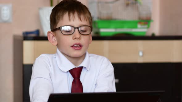 schoolboy in glasses sitting at home in front of a gadget participates in an online conference