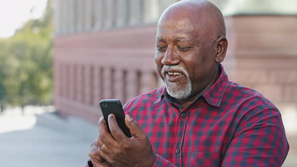 Happy Contented Senior Black Grandfather Man Making Video Call Looking at Smartphone Camera Showing