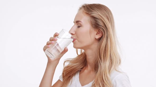 Young Beautiful Caucasian Blonde Girl Drinking Water From Glass and Smiling at Camera