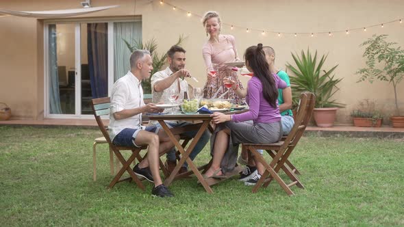 Friends Sharing Delicious Food During Dinner Meal at Home Garden in Summer Blond Woman Pouring Rose