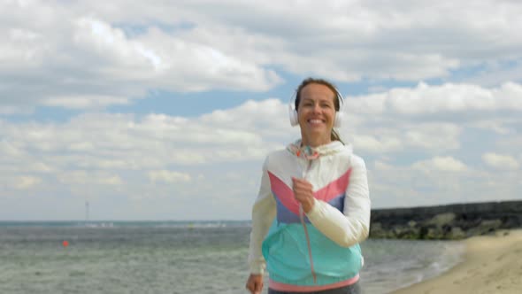 Smiling Woman with Headphones Running Along Beach 