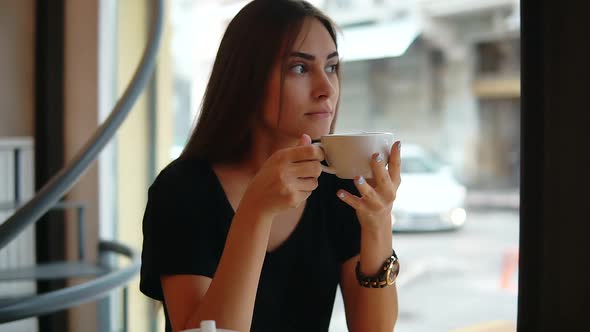 Beautiful Young Woman Dreaming with Cup of Hot Coffee Over Window in the Coffee Shop