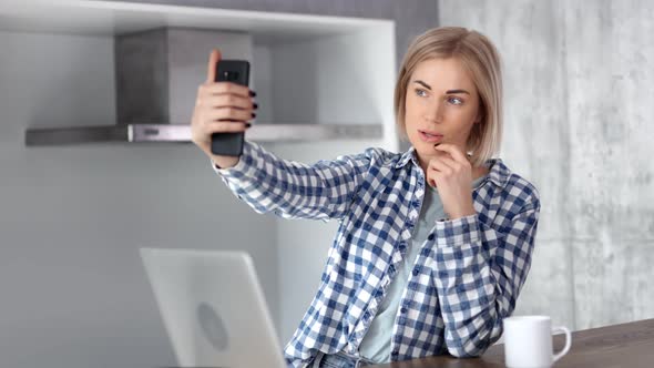 Pretty Young Casual Smiling Woman Taking Selfie Using Smartphone at Modern Home Kitchen