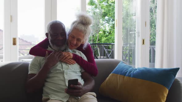 Mixed race senior couple using smartphone in the living room at home