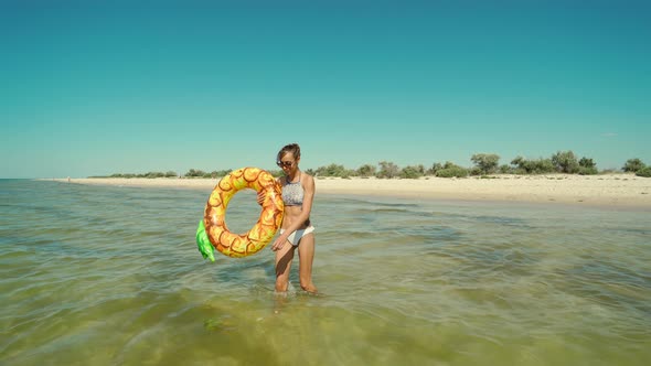 Portrait of Happy Smiling Young Woman in Sunglasses with Inflatable Pineapple Ring Walks in Sea