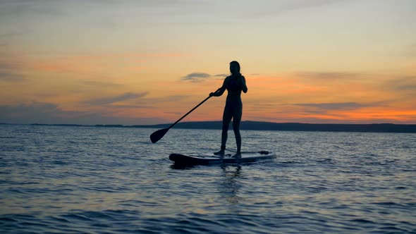 Picturesque Sunset with a Female Silhouette Sailing of a Paddleboard. Active Lifestyle Concept