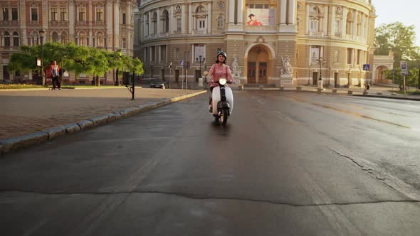 Young Beautiful Girl Riding Around City on Scooter at Sunrise