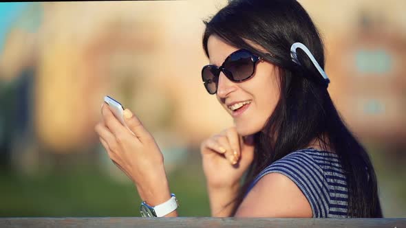 Young Brunette Straight Hair Woman in the Park Listening to Music with Headphones and Smartphone