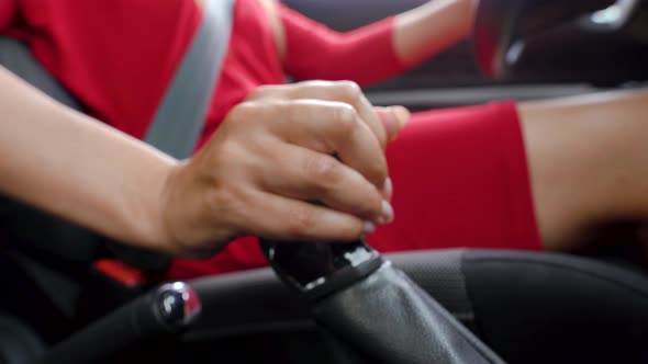 Closeup of Woman Driver in a Red Dress Fastens Her Seat Belt Changes Gear and Starts Moving
