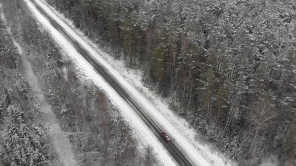 Red Car Drives Along a Picturesque Snow Covered Road in the Forest Countryside