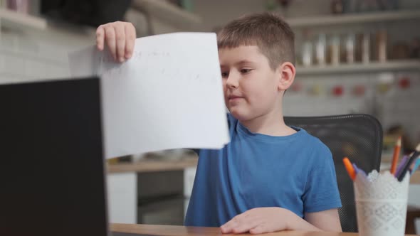 school child showing notebook to laptop screen while studying online at home