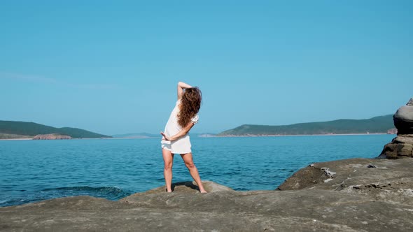 girl in a white sundress on the background of the sea on a bright sunny day