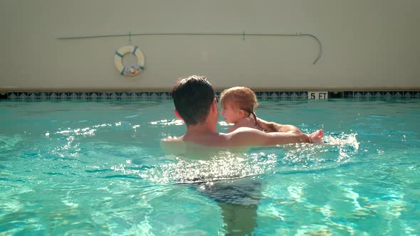 Cute Little Daughter and His Father Swimming in the Pool