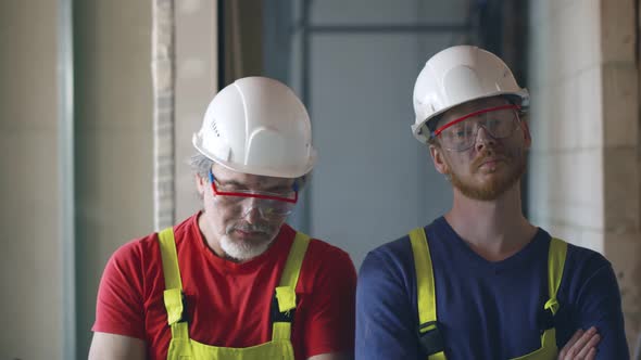 Two Builders with Arms Crossed Looking at Camera on Construction Site Background