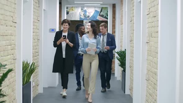 Four Positive Multiethnic Coworkers Walking in Office Corridor and Talking. Happy Colleagues