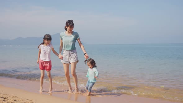 Asian family on vacation. Beautiful mother feeling relax playing on the sand sea with kid children.