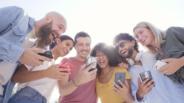 Low Angle of Multiracial Happy Group of Friends Using Phone and Smiling Together Outside