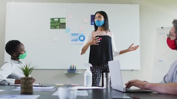 Asian woman wearing face mask giving presentation to her colleagues in meeting room at modern office