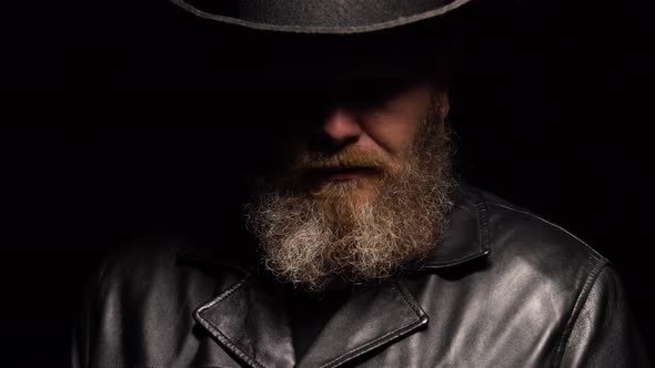 Portrait of Man with a Beard in a Leather Coat and an Original Hat on a Black Studio Background