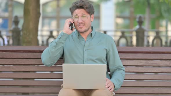 Middle Aged Man Talking on Phone while using Laptop