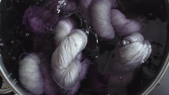 Topdown view of a pot as someone mixes skeins of yarn in it with a spoon in slow motion