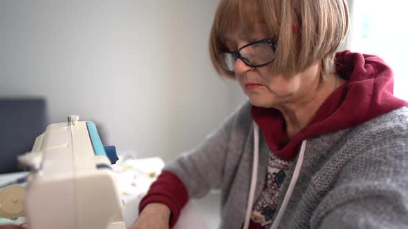 Pensioner Woman Wearing Glasses Sews Home Textiles on a Sewing Machine