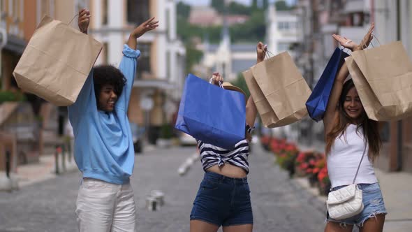 Excited Girls Rising Shopping Bags Up on Street