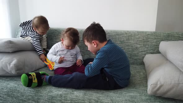 Big brother playing with his sisters twins on couch in living room. Happy family.